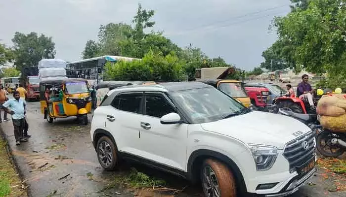 రోడ్డుపై అడ్డంగా పడిపోయిన చెట్లు.. కిలోమీటరు వరకు నిలిచిపోయిన వాహనాలు. రోడ్డుపై అడ్డంగా పడిపోయిన చెట్లు.. కిలోమీటరు వరకు నిలిచిపోయిన వాహనాలు.